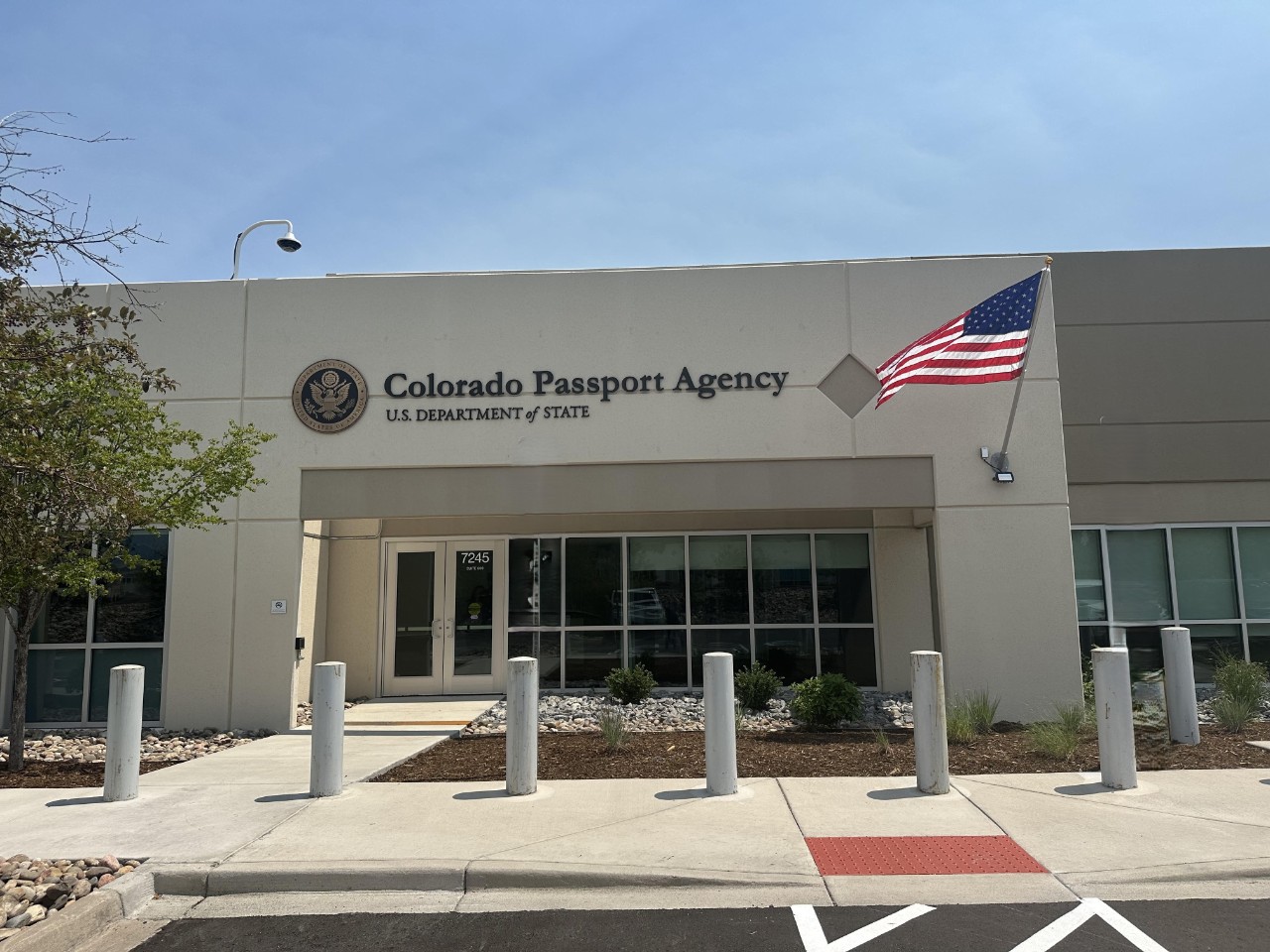 The Colorado Passport Agency.  It is a single-story building with an American flag, “Colorado Passport Agency” in large text above glass doors, and concrete bollards in front of the entrance.