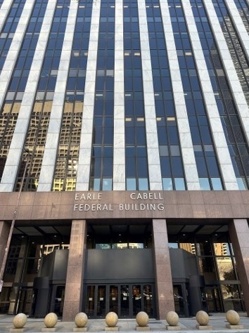 Exterior of the front entrance to the Dallas Passport Agency. It is in a rectangular office building with horizontal columns of windows. The doors sit below a sign that says “EARL CABELL FEDERAL BUILDING”